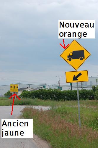 Photo où on voit 2 panneaux, celui à l’avant-plan avec le nouveau orange, celui à l’arrière-plan avec le vieux jaune